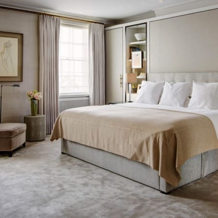 Janine Stone & Co interior design — central London townhouse master bedroom with neutral palette, bespoke upholstered headboard, classical sash window and framed pencil portrait.