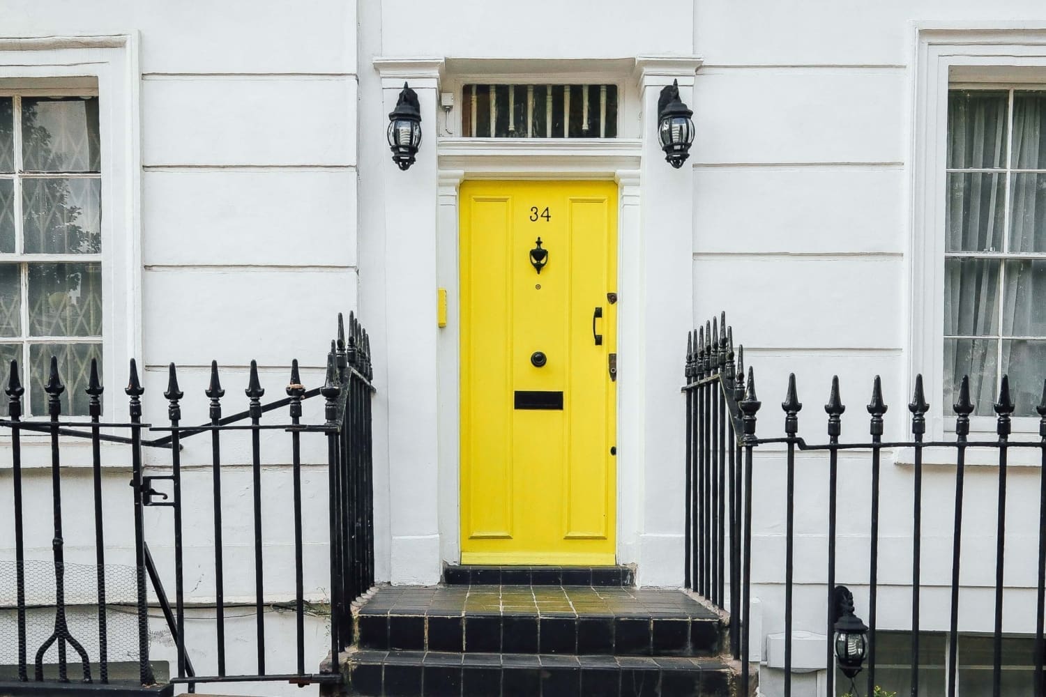 Janine Stone & Co — yellow front door of central London townhouse with black wrought-iron railings and traditional lantern coach lights, illustrating an off-market central London home purchase.